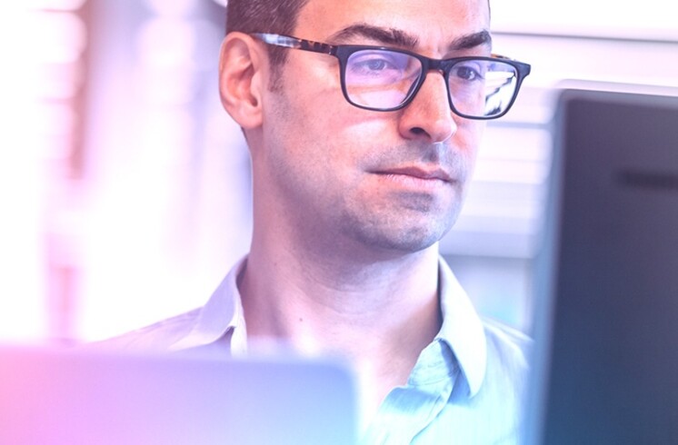 A man in glasses is looking at a computer screen